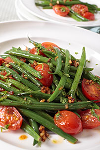healthy warm green bean salad with cherry tomatoes and walnuts on white plate