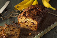 slice cut from loaf of banana chocolate chip sour cream bread with four bananas in background_498712054