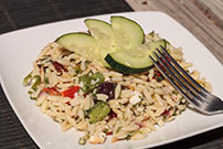 greek pasta salad made with orzo cucumbers on white plate 577341354