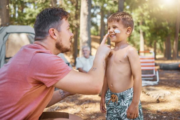 A father applying sunscreen to his son's face while on a family camping trip.