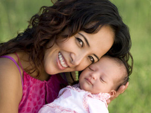 A young hispanic woman cradles her newborn baby against her cheek and smiles