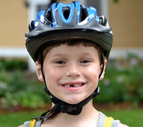 A boy who just lost his front took, proudly shows how to wear a bike helmet correctly.