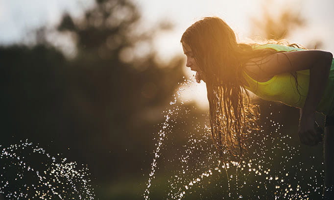 girl drinking water from sprinkler