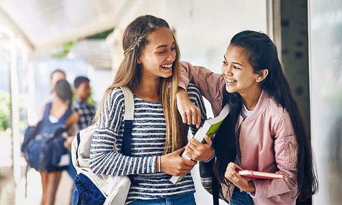 Middle school girls laugh together in a school hallway