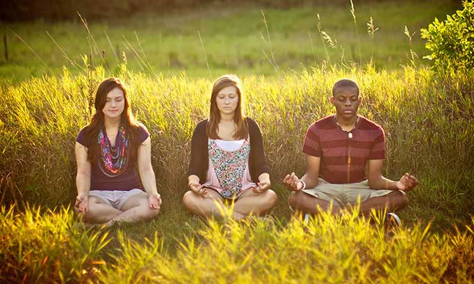Three teens use guided imagery while seated in a meditation pose