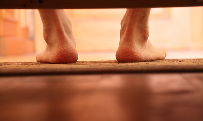 Bare feet on the floor as man steps out of bed, an example when you might hear cracking and popping noises in joints. 