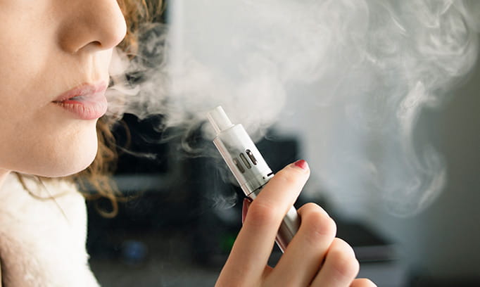 A young woman is shown vaping, or inhaling the vapor of an e-cigarette