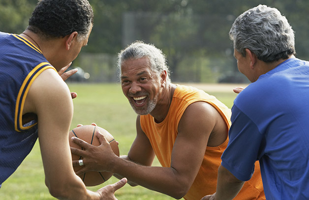 Three older men playing football in a park experiencing the benefit of exercise.