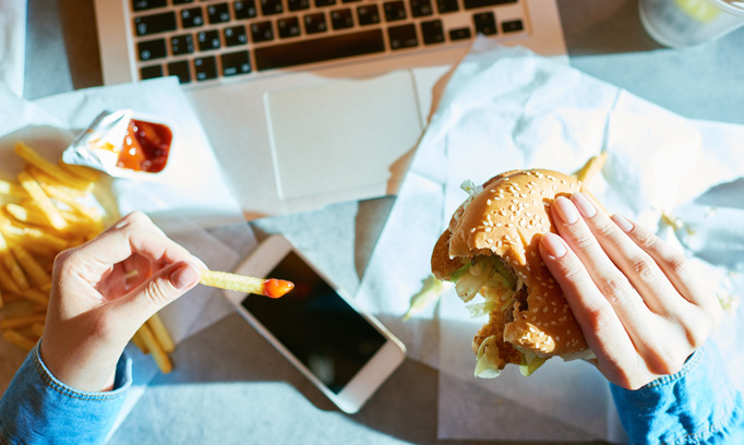 Person eats junk food while looking at a smartphone, a poor eating habit that can be helped by mindfulness