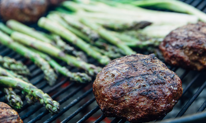 burgers and asparagus cooking on a grill