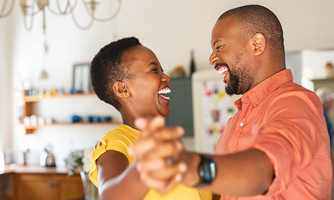Laughing middle-aged African American couple enjoy staying fit by dancing together in their kitchen.