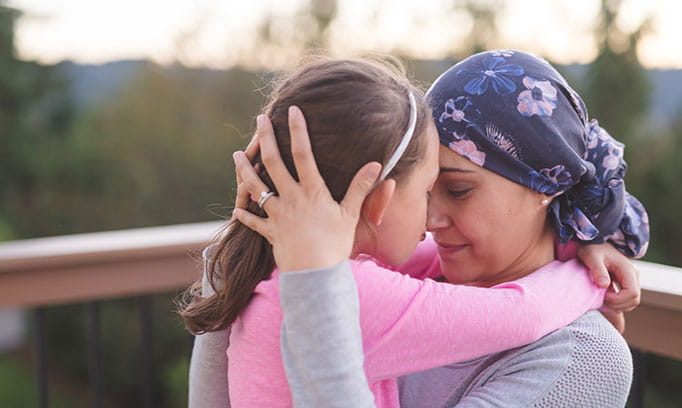 Two women hug, one appears to be undergoing cancer treatment  as she's wearing a blue bandanna on her head