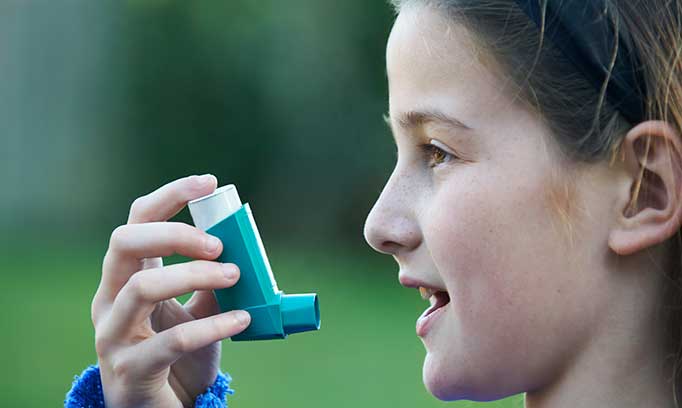 Girl with asthma holds an inhaler near her mouth