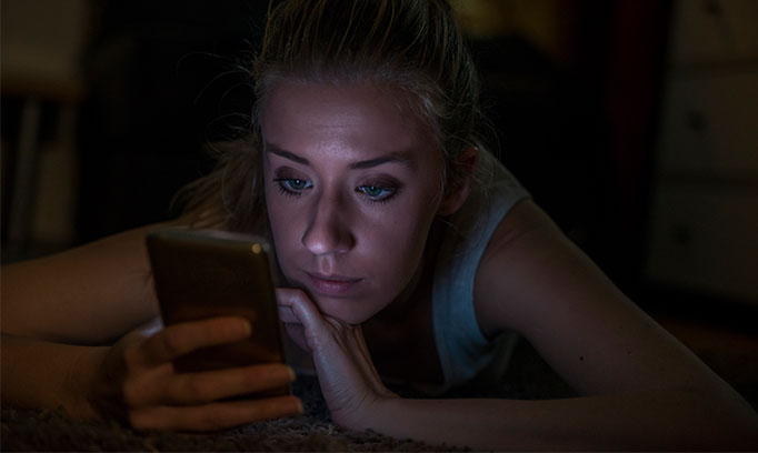 Young woman using phone at night, a potential contributor to sleep loss.