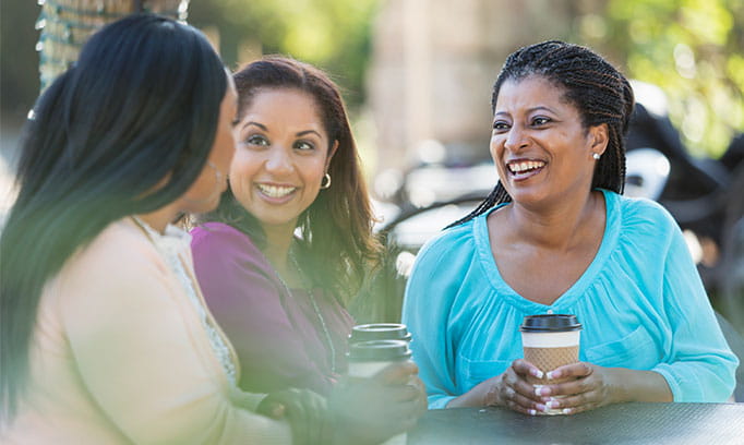 Three woman sitting outside around a table discussing 3D mammograms