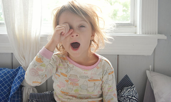Young child who just woke up, is yawning, and rubbing their eye because they are experiencing symptoms of pink eye.