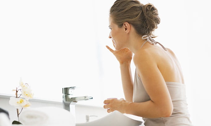 Woman applying moisturizer to her face for dry skin.