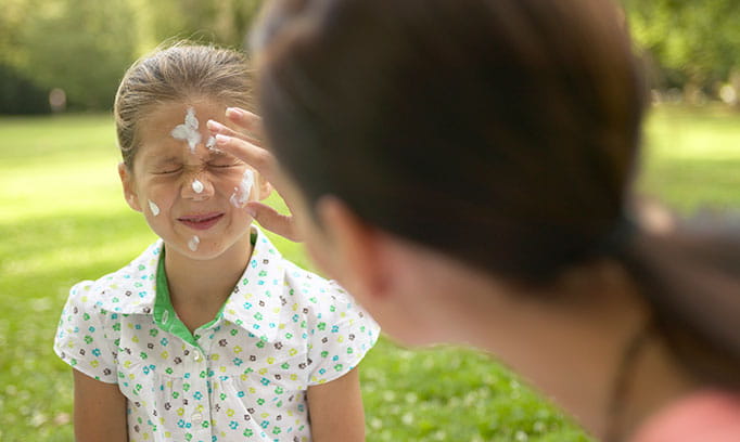 A mother applying sunscreen to their daughter’s face to protect them from the suns UV rays
