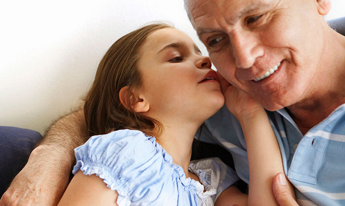 Young girl whispers in grandfather's ear to illustrate impact of hearing loss on seniors.