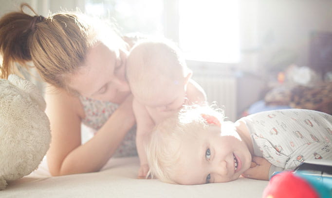 Mom watching an older sibling play with the new baby