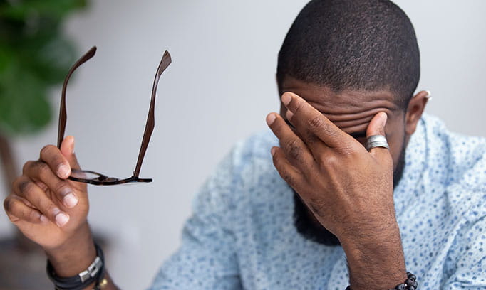 A man in distress over a stroke in his family touching his forehead with one hand and holding his glasses in the other