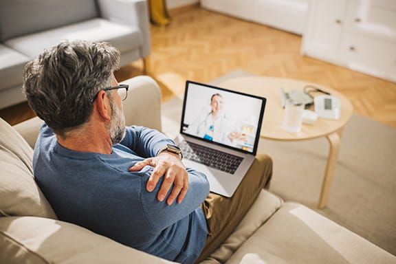 Man with shoulder pain on a virtual video call on his laptop with a doctor.