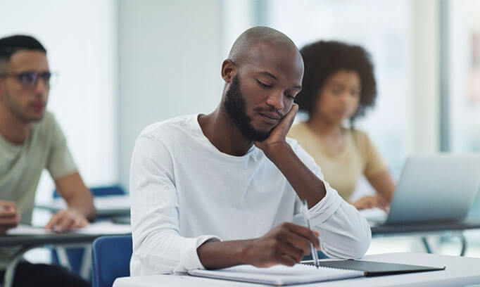 A man with adult ADHD in a classroom staring at his desk struggling to focus.