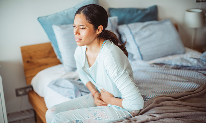Woman sitting on her bed with pain from food poisoning symptoms