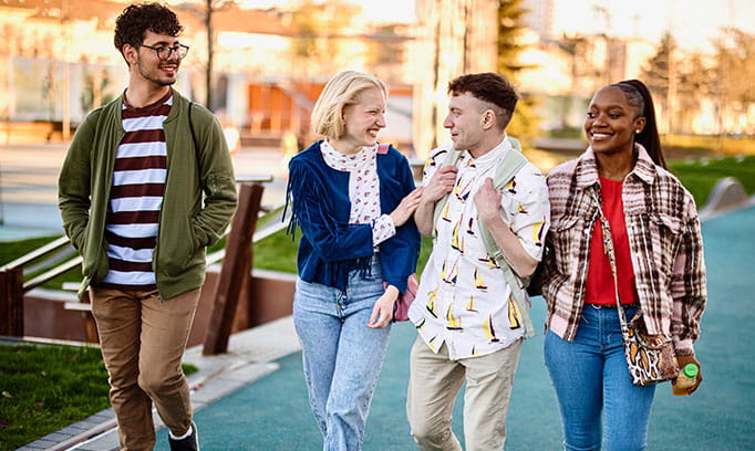 Young adults walking outside and smiling at their friend. 