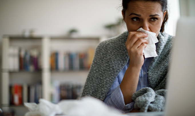 A woman wrapped in a blanket blowing her nose into a tissue suffering from a sinus infection 