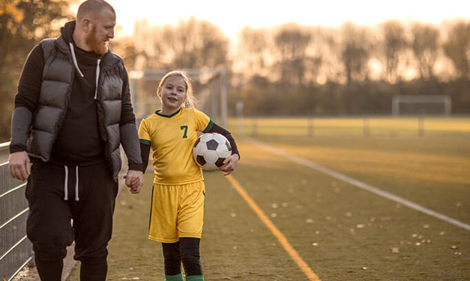 A dad walking with his student-athlete daughter who is in a soccer uniform and hold a soccer ball