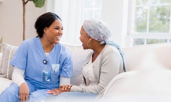 A cancer nurse navigator sitting on a white couch with a female cancer patient
