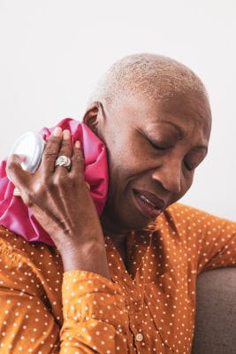 female applying a cold compress to side of neck as one way to manage pain after cancer surgery