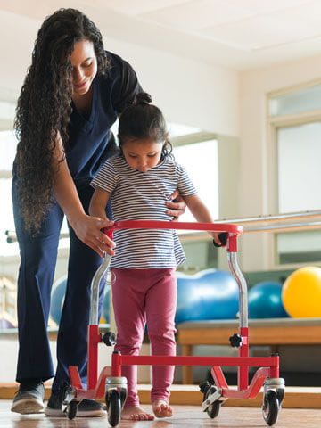 little girl being helped by physical therapist to walk with walker