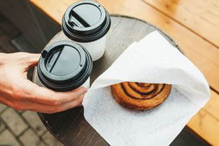 Two coffees in to-go cups and a pastry in paper.