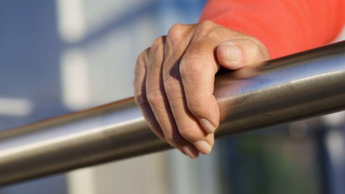 Low angle view of an unrecognizable, senior adult, woman grasping a stainless steel safety rail with her right hand.