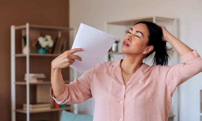 A woman fanning herself to manage a hot flash, a common symptom of perimenopause and menopause often treated with hormone therapy. 