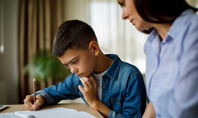 child with ADHD studying while mother looks on 