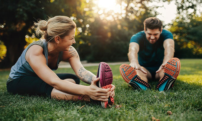 young 20 something woman and man stretch on grass to warm up before exercise
