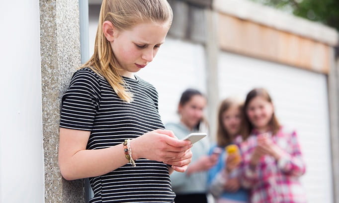teen girl checks phone as she worries about a bully
