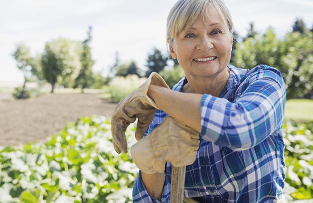 Older female gardener leaning on a shovel handle.