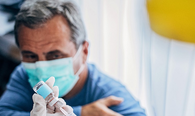 man wearing face cover pulls up shirt sleeve as he prepares for a vaccine injection 