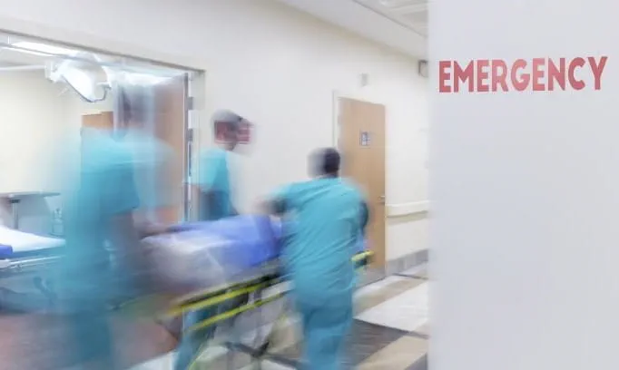 three people in scrubs racing a gurney into the emergency room