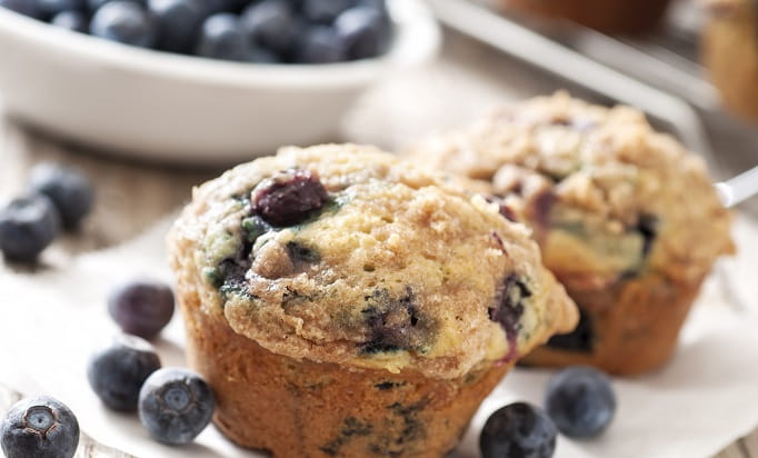 two blueberry muffins on plate with pint of blueberries next to it