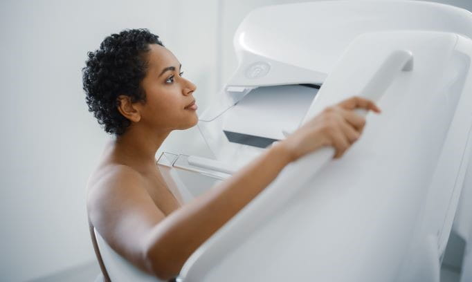 female extending right arm to hold handle of mammogram machine