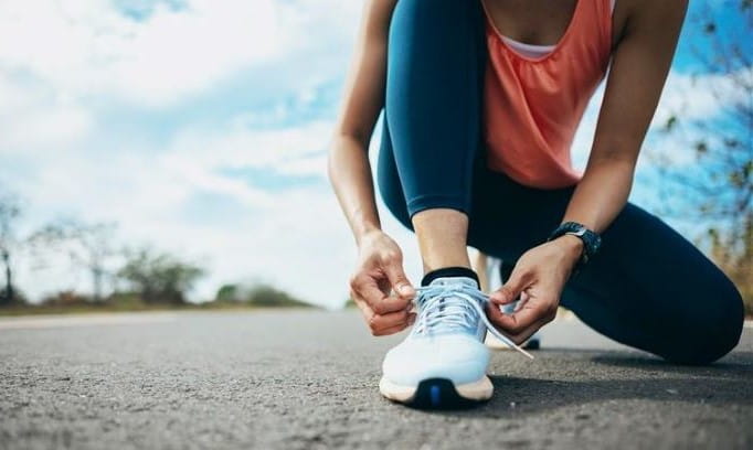 woman kneeling on blacktop to tie running shoe 