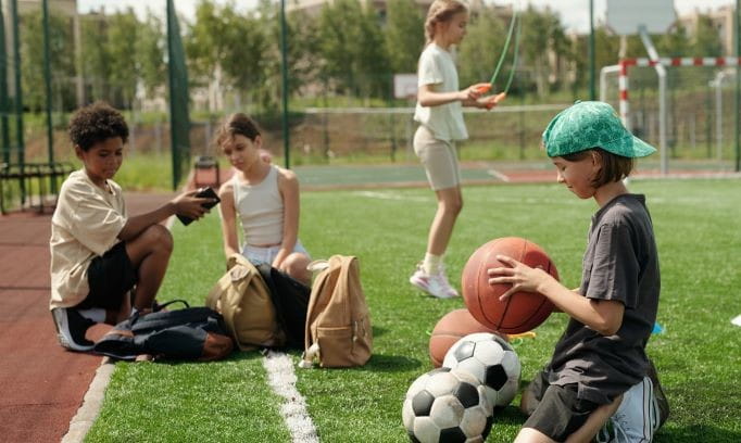 four school aged children on athletic field surrounded by sports equipment