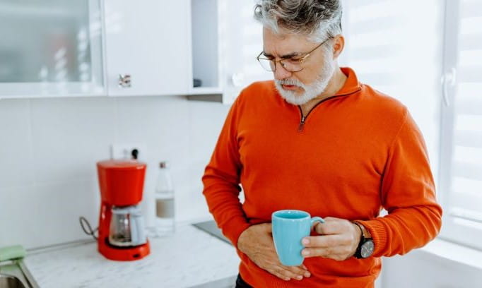 grimacing man with one hand on stomach because of food poisoning and other hand holding coffee cup