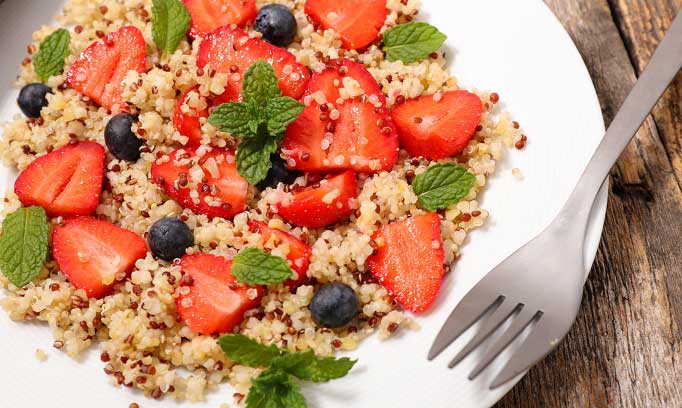 strawberry blueberries and quinoa salad in shallow white bowl with fork resting on right side rim