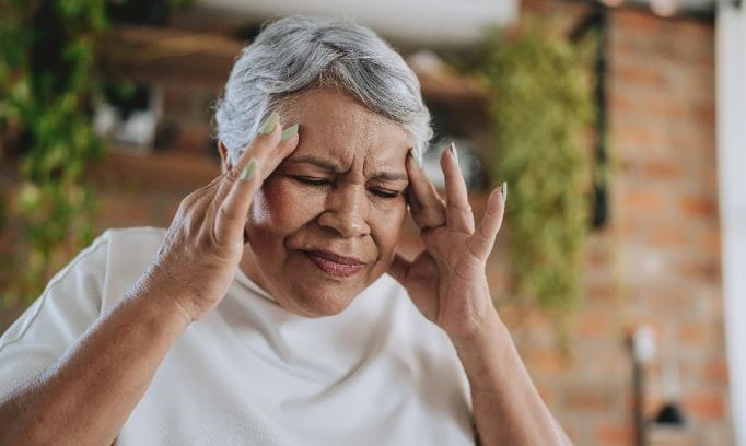 woman with short gray hair puts fingers to temples and grimaces with pain